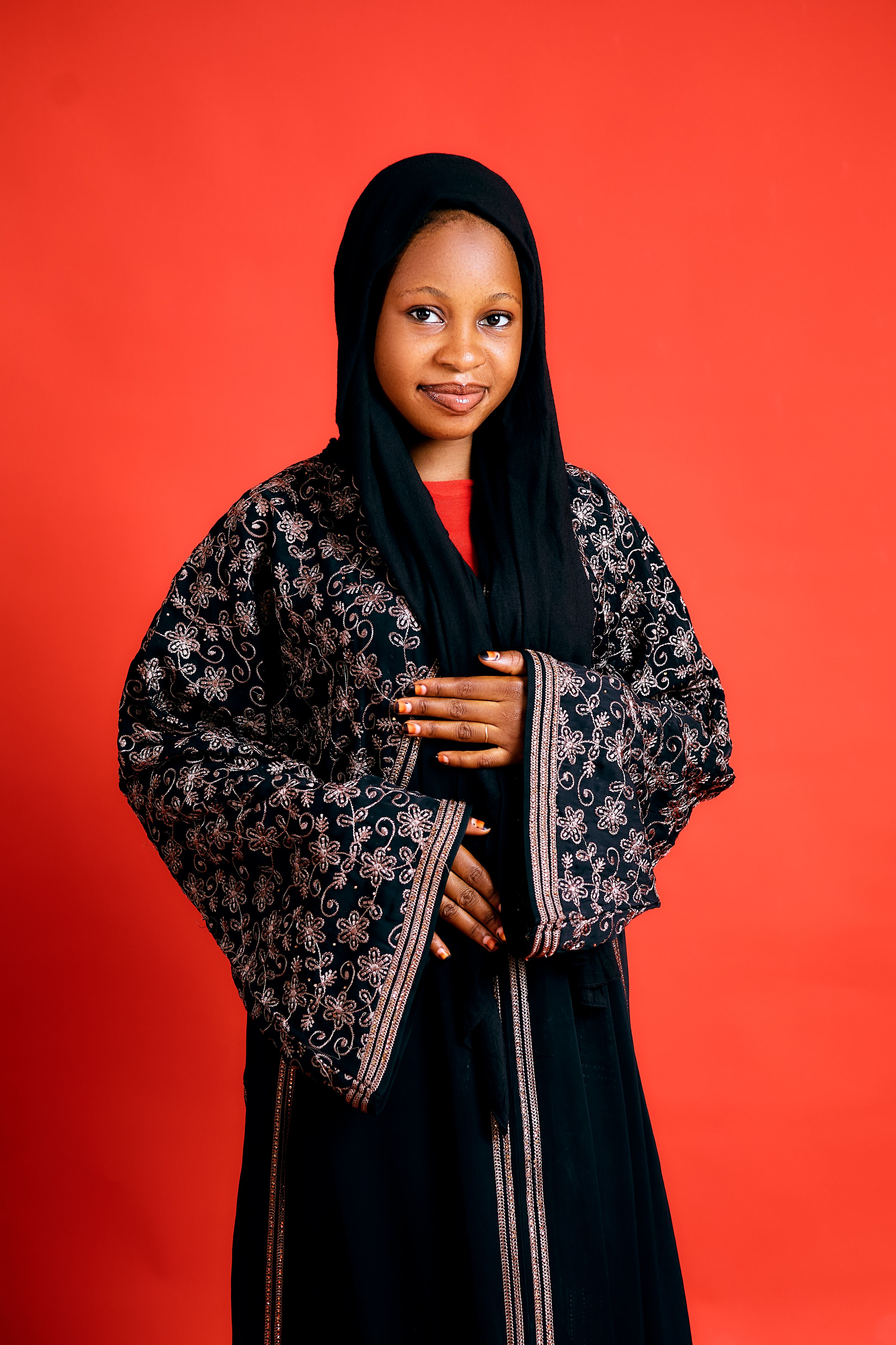 Portrait of a young woman wearing a black traditional embroidered garment on red backdrop.