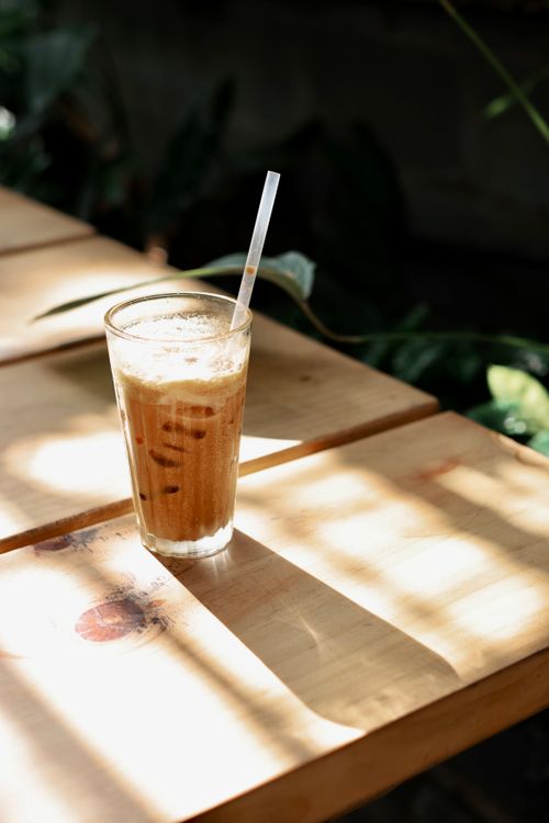 Free Cool iced coffee glass with straw on sunlit wooden table. Stock Photo
