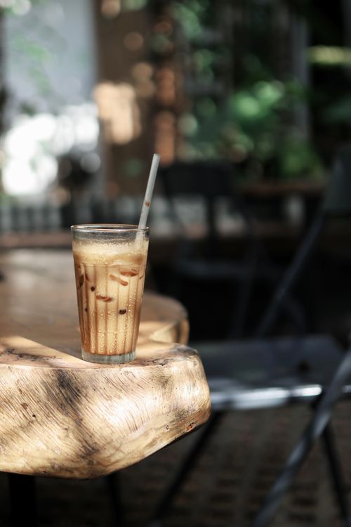 Free A glass of iced coffee sits on a sunlit wooden table in a cozy outdoor cafe. Stock Photo