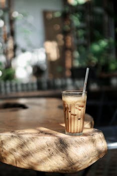 A refreshing glass of iced coffee with straw on a sunlit wooden table.