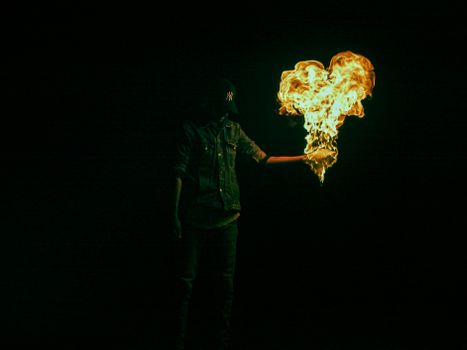 A person in a dark setting holding a flame shaped like a heart, creating a dramatic and mysterious atmosphere.