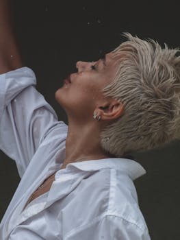 Profile of a woman with short blond hair wearing a white shirt, captured in a moody, dramatic tone.