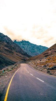 Winding road through Kargil mountains under a cloudy sky, showcasing Ladakh's rugged beauty.