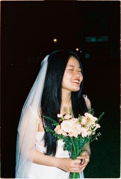 Smiling bride in wedding dress holding bouquet, celebrating at night.