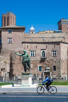 A cyclist rides past an ancient statue near historical buildings in Rome, Italy.