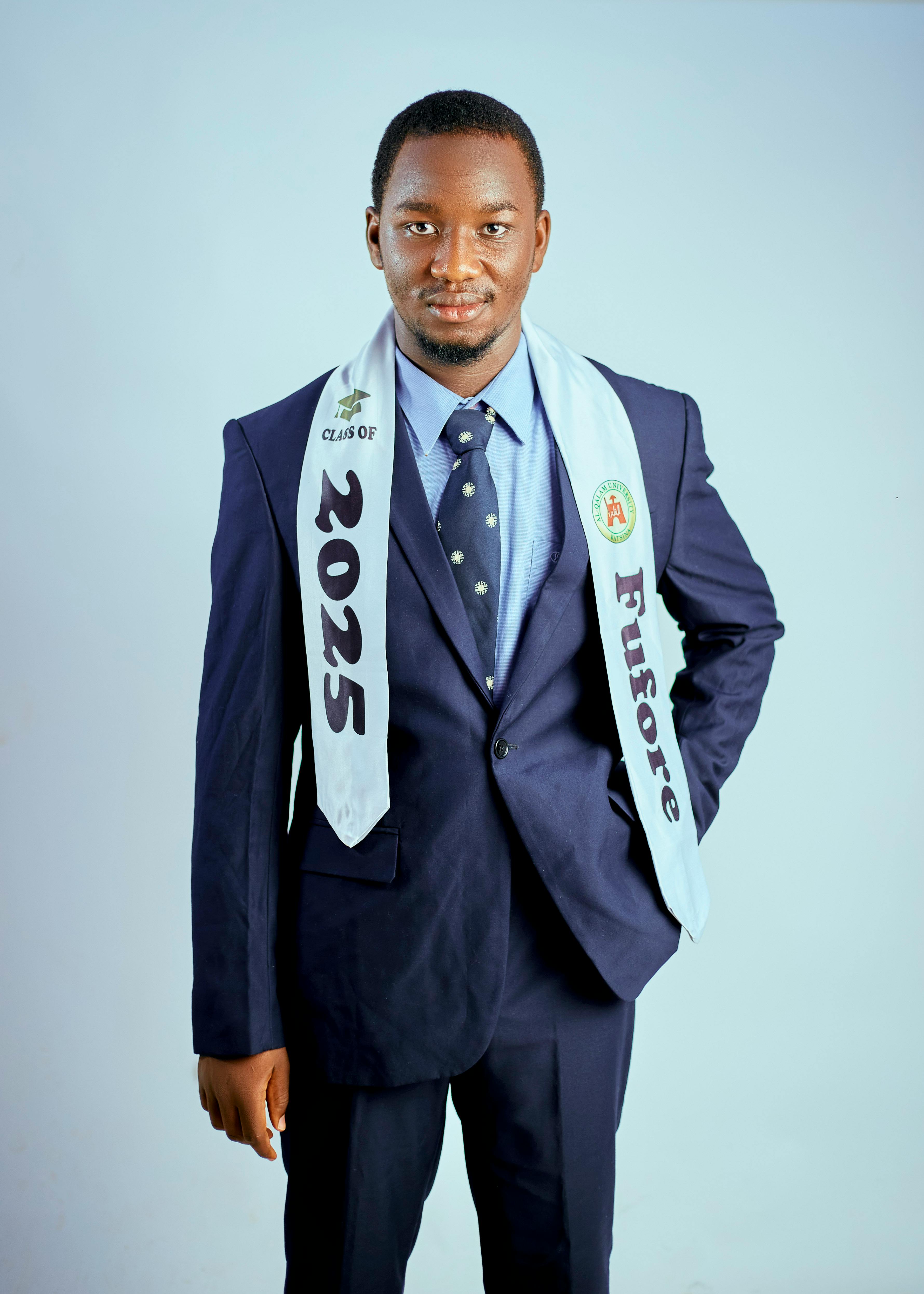 Young adult male in navy suit with Class of 2025 sash, standing confidently.