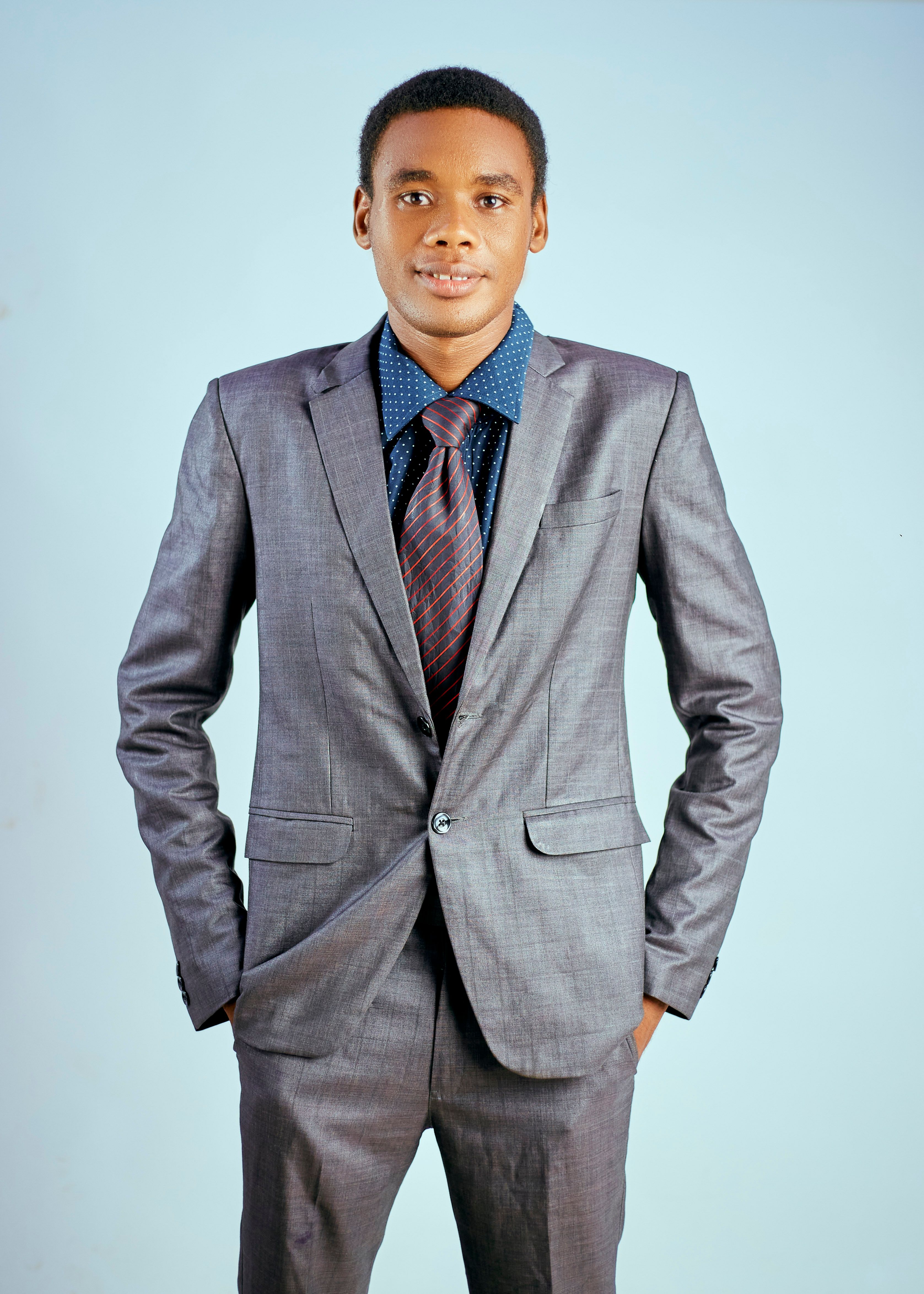Well-dressed man in a gray suit posing confidently against a blue backdrop.