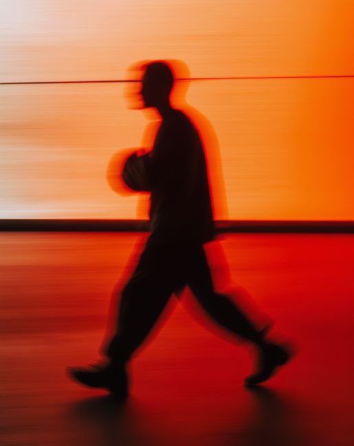 Artistic silhouette of a person walking in motion blur against a vivid orange backdrop, evoking a cinematic feel.