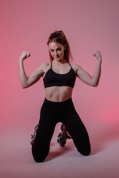 Confident woman in athletic wear flexes muscles in a vibrant studio setting.