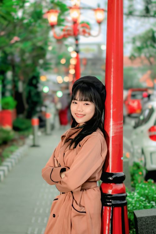Free Smiling woman leaning on bright red post in vibrant urban street. Daytime setting. Stock Photo