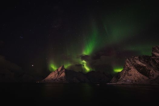 Breathtaking view of aurora borealis illuminating snow-covered peaks at night.