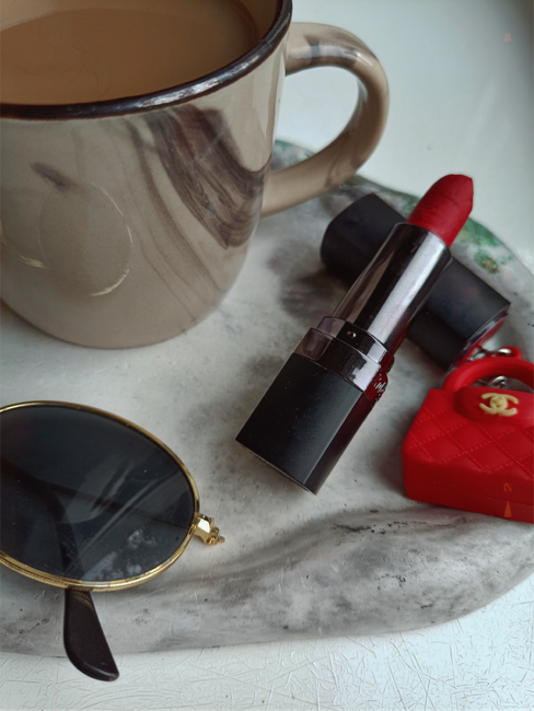 Stylish flat lay of coffee, lipstick, sunglasses, and red accessories.