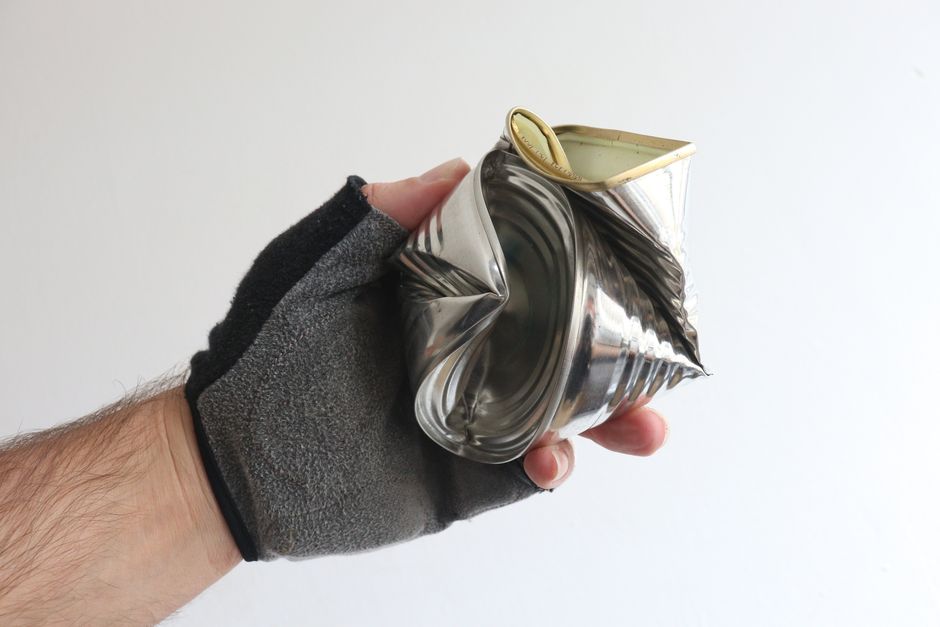 A gloved hand holding a crushed tin can showcases recycling and waste management.
