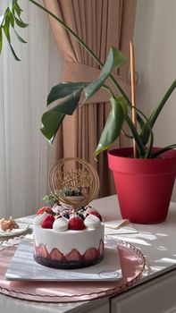 Delicious birthday cake with strawberries in a bright room alongside a houseplant.