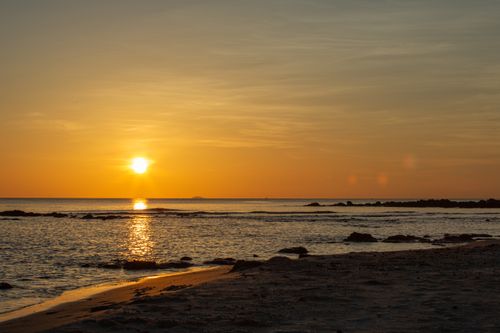 Free Peaceful sunrise over a sandy beach with warm golden tones reflecting on the ocean. Stock Photo