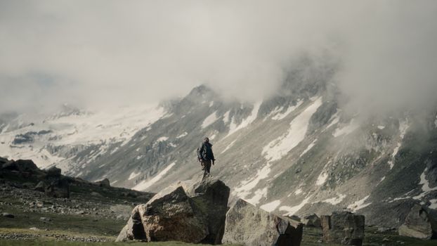 A lone hiker stands on a rock amidst snowy mountains and mist, reflecting solitude and adventure.