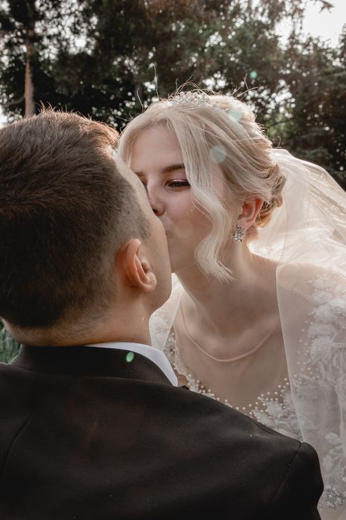 Free A bride and groom share a tender kiss outdoors, capturing a romantic wedding moment. Stock Photo