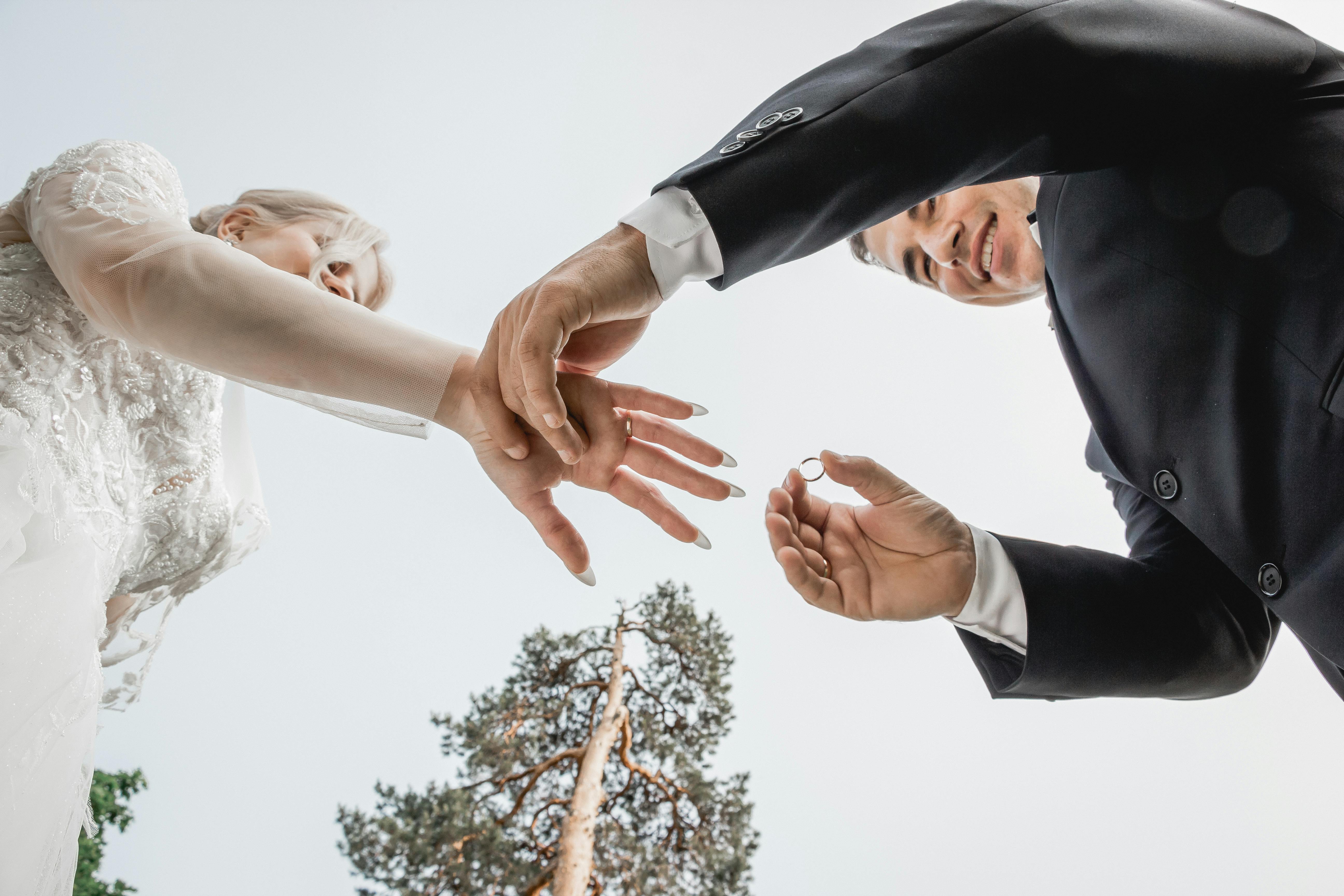 Couple exchanging wedding rings outdoors under a clear sky. - marital resentment