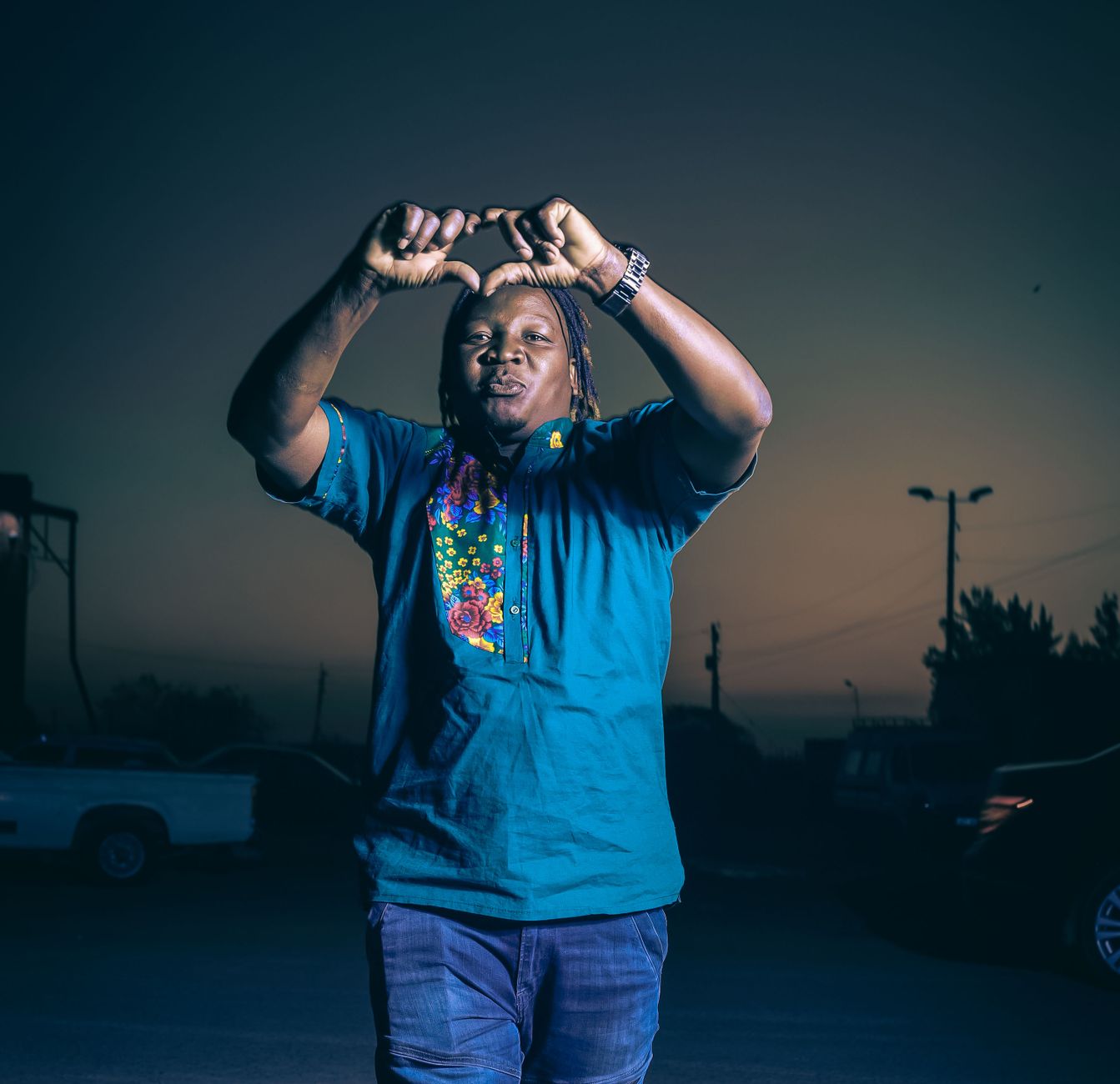 Outdoor portrait of a person making a hand gesture at twilight in South Africa, wearing traditional clothing.