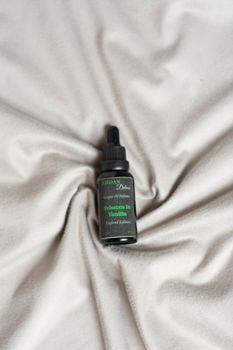 Black essential oil dropper bottle on soft beige fabric, luxurious feel.
