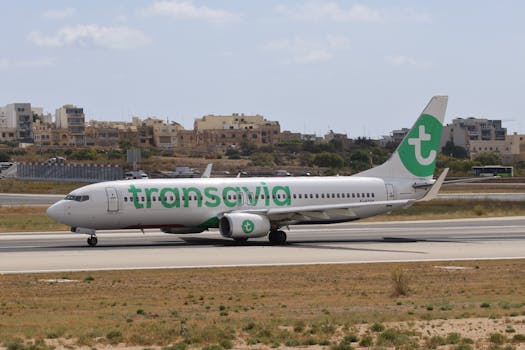 Transavia aircraft taxiing on the runway with a cityscape backdrop under a bright sky.