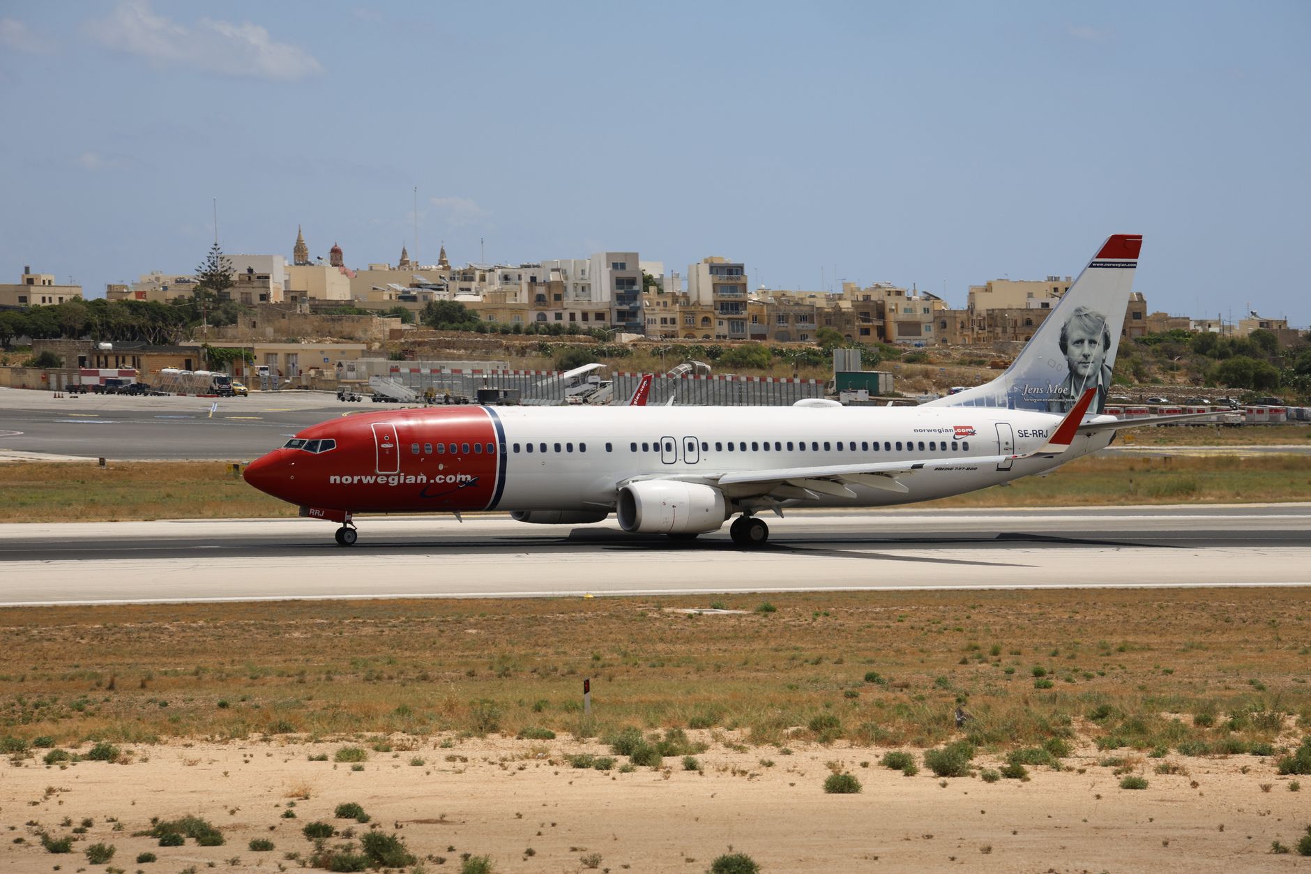 Norwegian Boeing 737 aircraft on runway with scenic backdrop, clear sky.