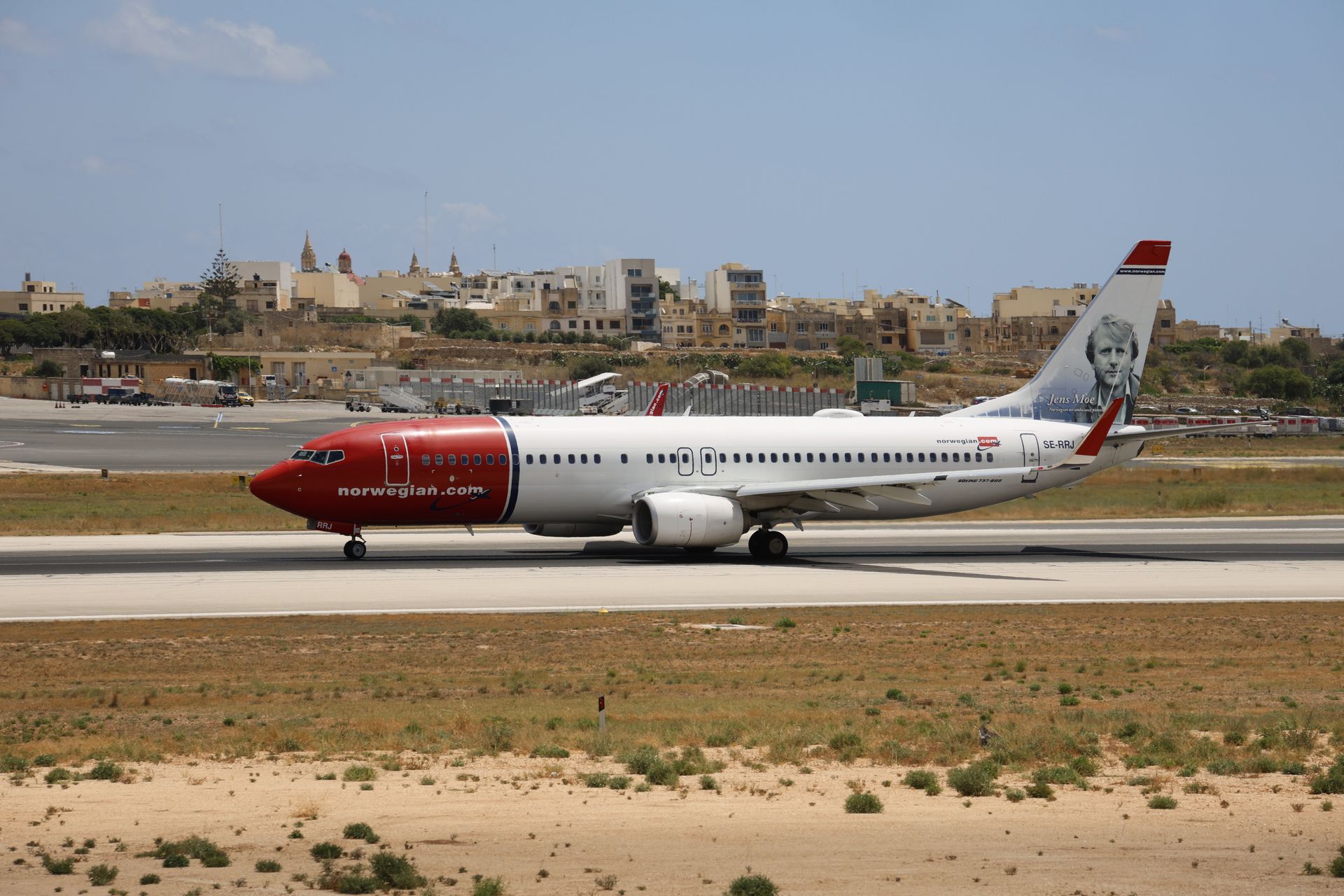 Norwegian Boeing 737 aircraft on runway with scenic backdrop, clear sky.