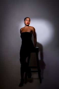 Elegant woman in black dress modeling under spotlight, creating a moody and dramatic effect.