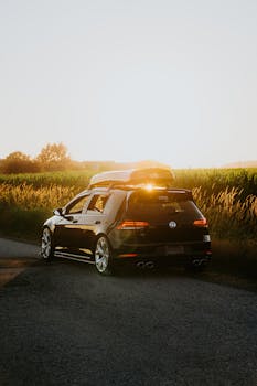 A sleek black car parked on a rural road at sunset, perfect for travel or adventure themes.