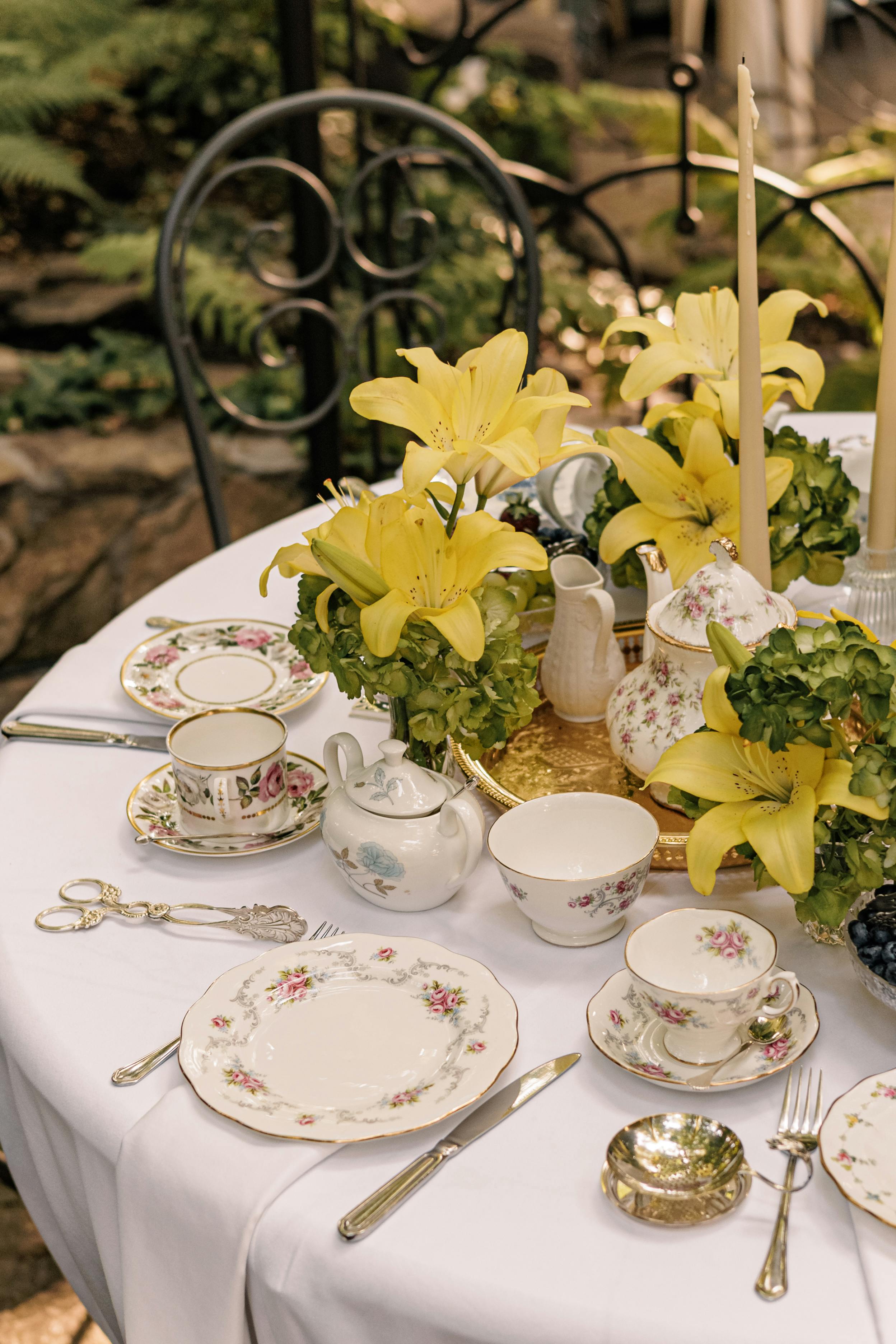 Beautifully arranged outdoor tea party table with yellow lilies and fine china.