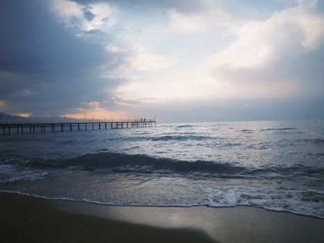 Tranquil sunset view over Lake Issyk-Kul with waves lapping the shore and a distant pier.