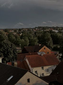 A scenic view of a suburban neighborhood with red-tiled roofs surrounded by lush greenery under a cloudy sky.