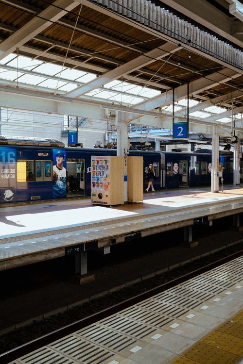 Free Sunlit platform at a Japanese train station showing modern architecture and train cars. Stock Photo