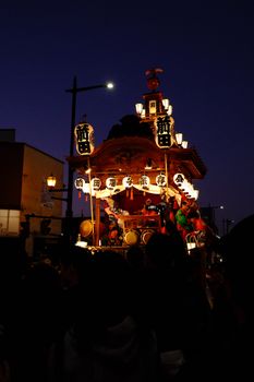 A traditional Japanese festival float glowing under twilight sky, showcasing vibrant cultural decorations.