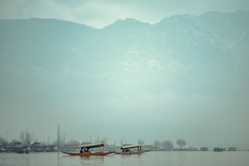 Two traditional shikara boats on a serene misty lake