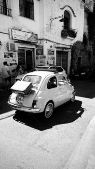 Black and white image of a vintage Fiat on a sunny street in Positano, Italy.