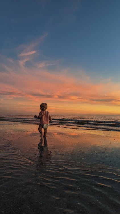 Child in White Shorts Walking on Beach during Sunset