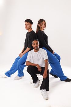 Three young adults in casual outfits pose against a white studio background, showcasing modern fashion styles.