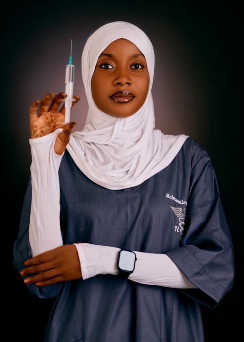 Free Portrait of a female healthcare worker in uniform holding a syringe confidently against a dark background. Stock Photo