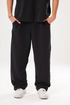 A close-up of casual black pants and white sneakers against a white background.