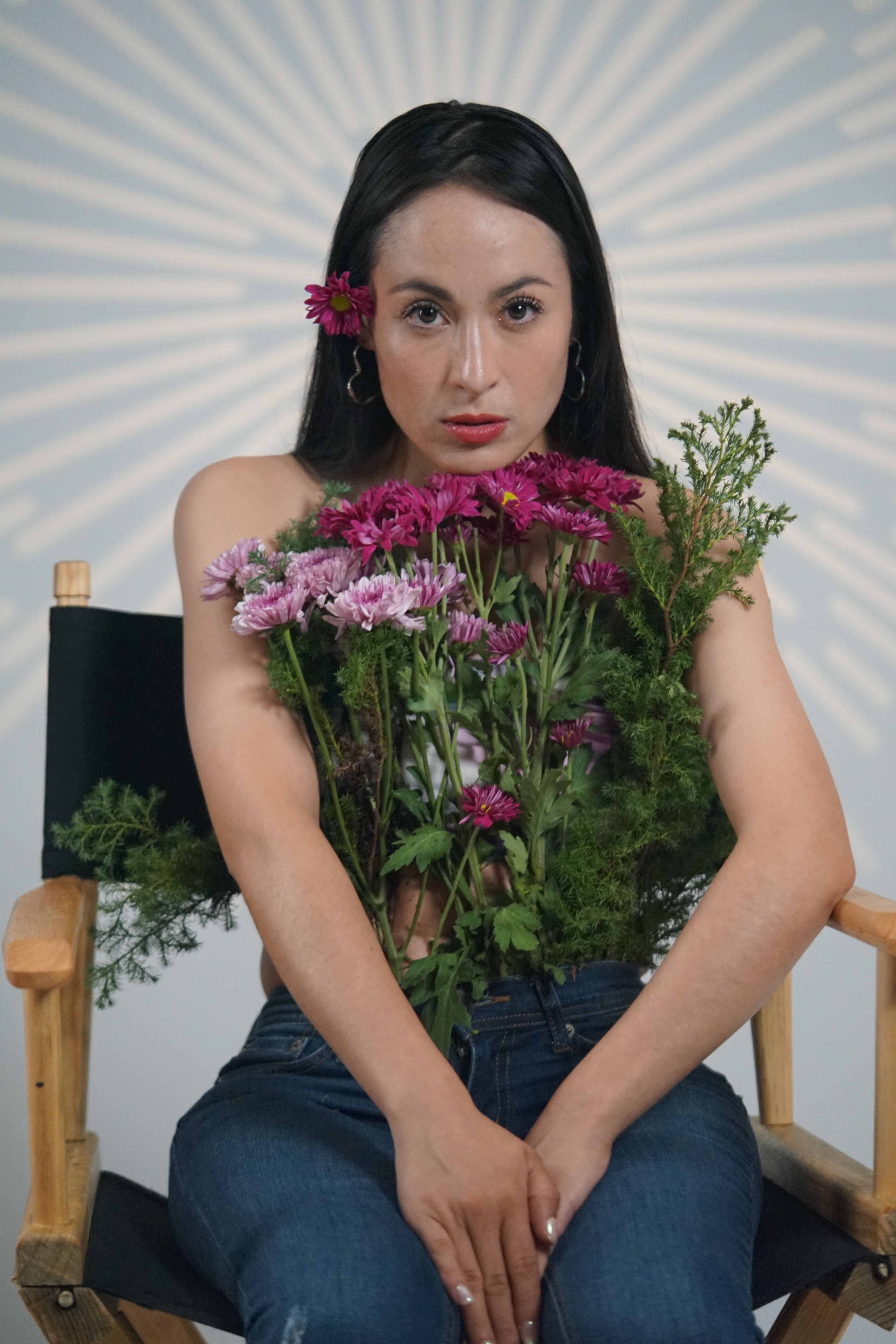 Portrait of a woman holding purple daisies and greenery while sitting in a director's chair.