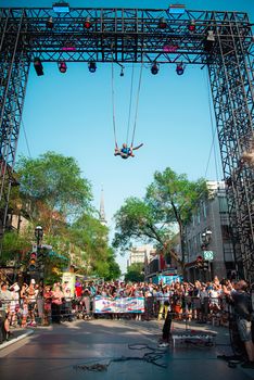 A daring performer swings high above a crowd at an outdoor summer festival.