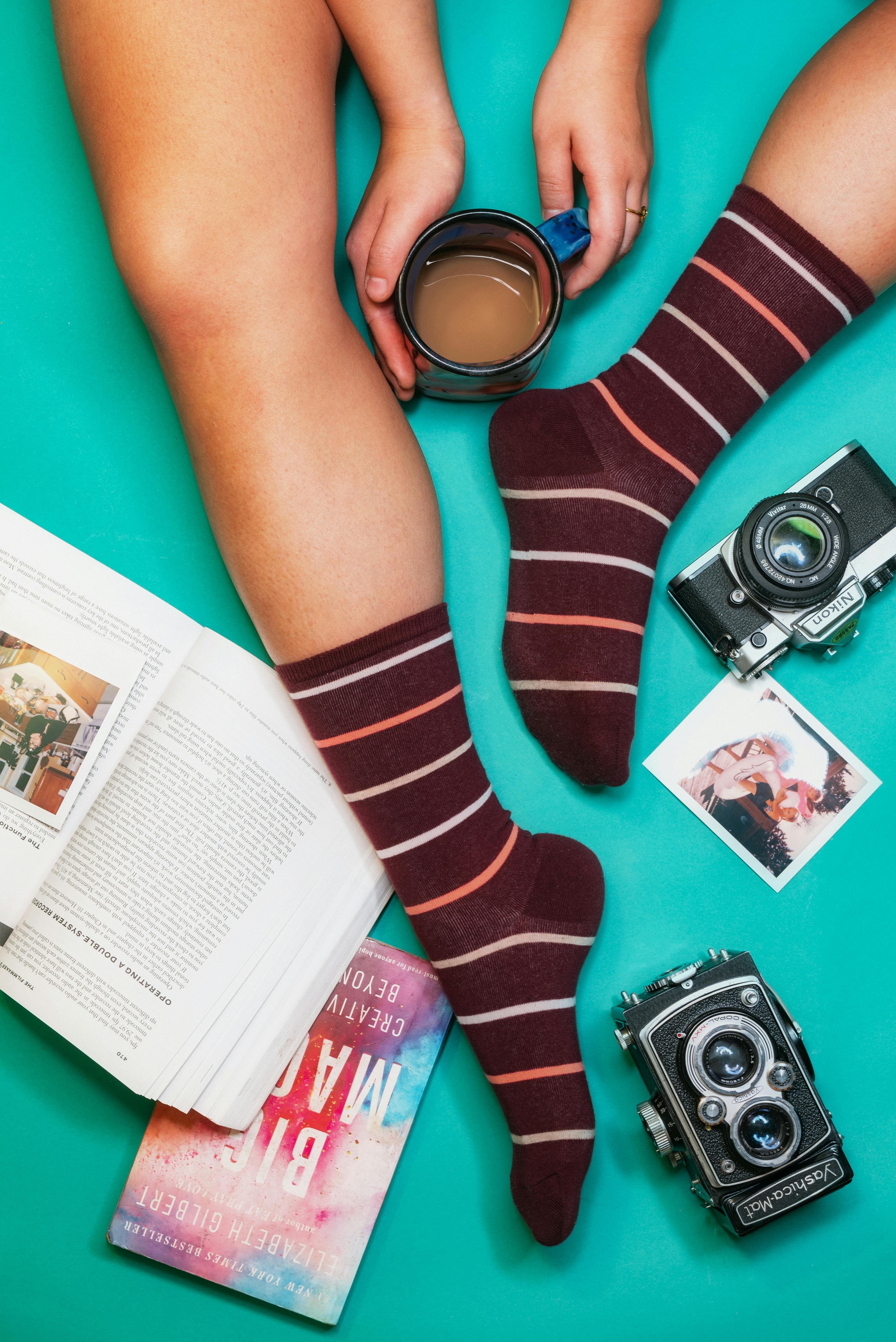 Cozy setup with striped socks, vintage cameras, and coffee for a perfect reading break.
