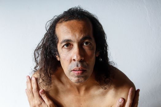 Captivating close-up portrait of a male adult with intense gaze, curly hair, and bare shoulders.