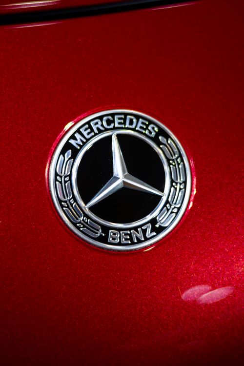 Free Detailed view of the iconic Mercedes-Benz logo on a sleek red car, highlighting luxury and automotive design. Stock Photo