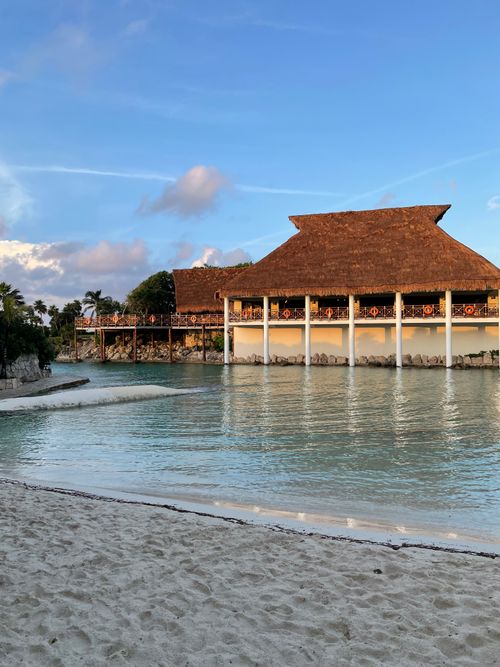 Free Calm beachfront resort scene at sunset with thatched-roof building, inviting tropical paradise. Stock Photo