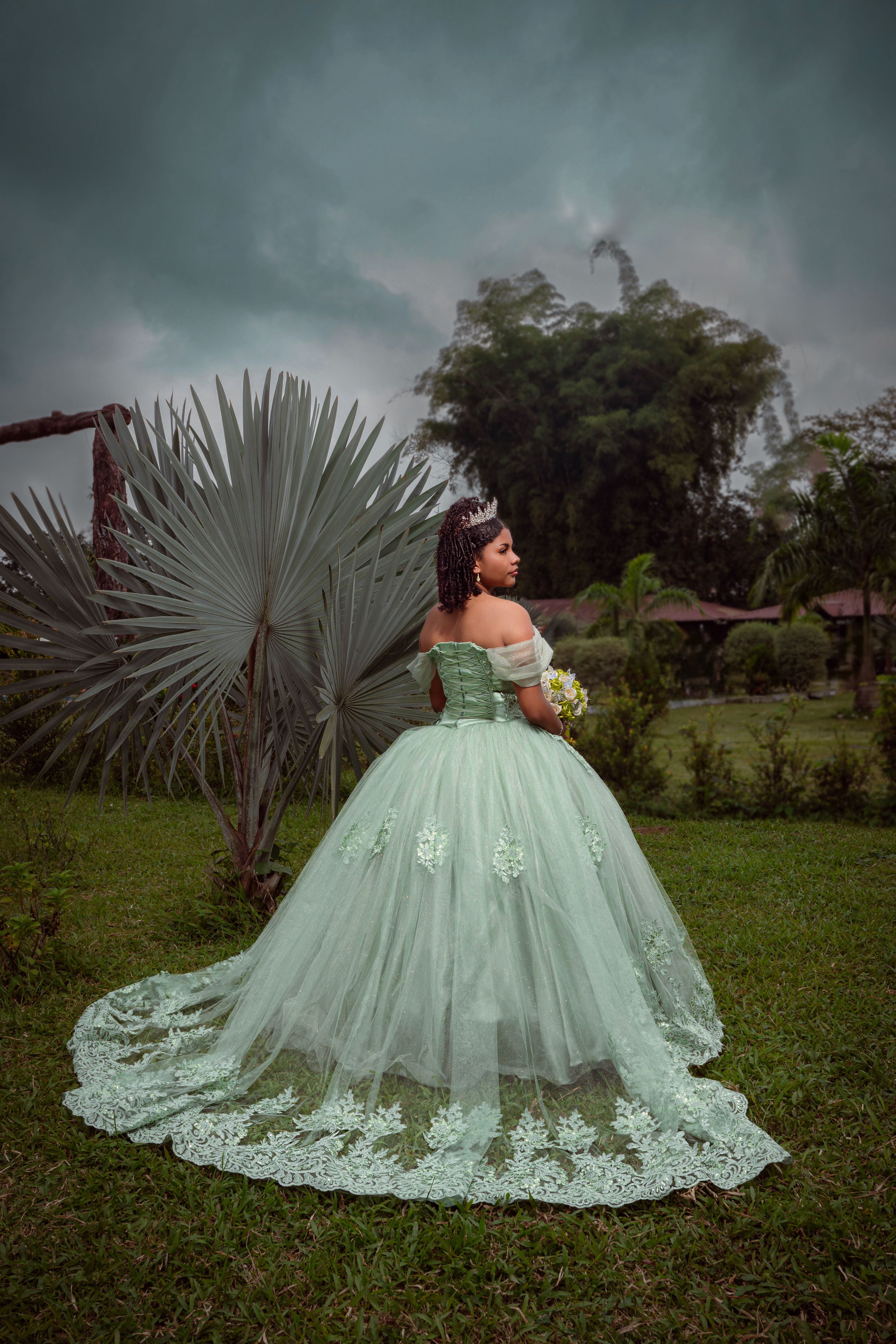 A young girl in a quinceañera dress stands in a tropical Ecuadorian garden.