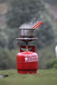 Steam rises from a pot on a portable gas stove outdoors.