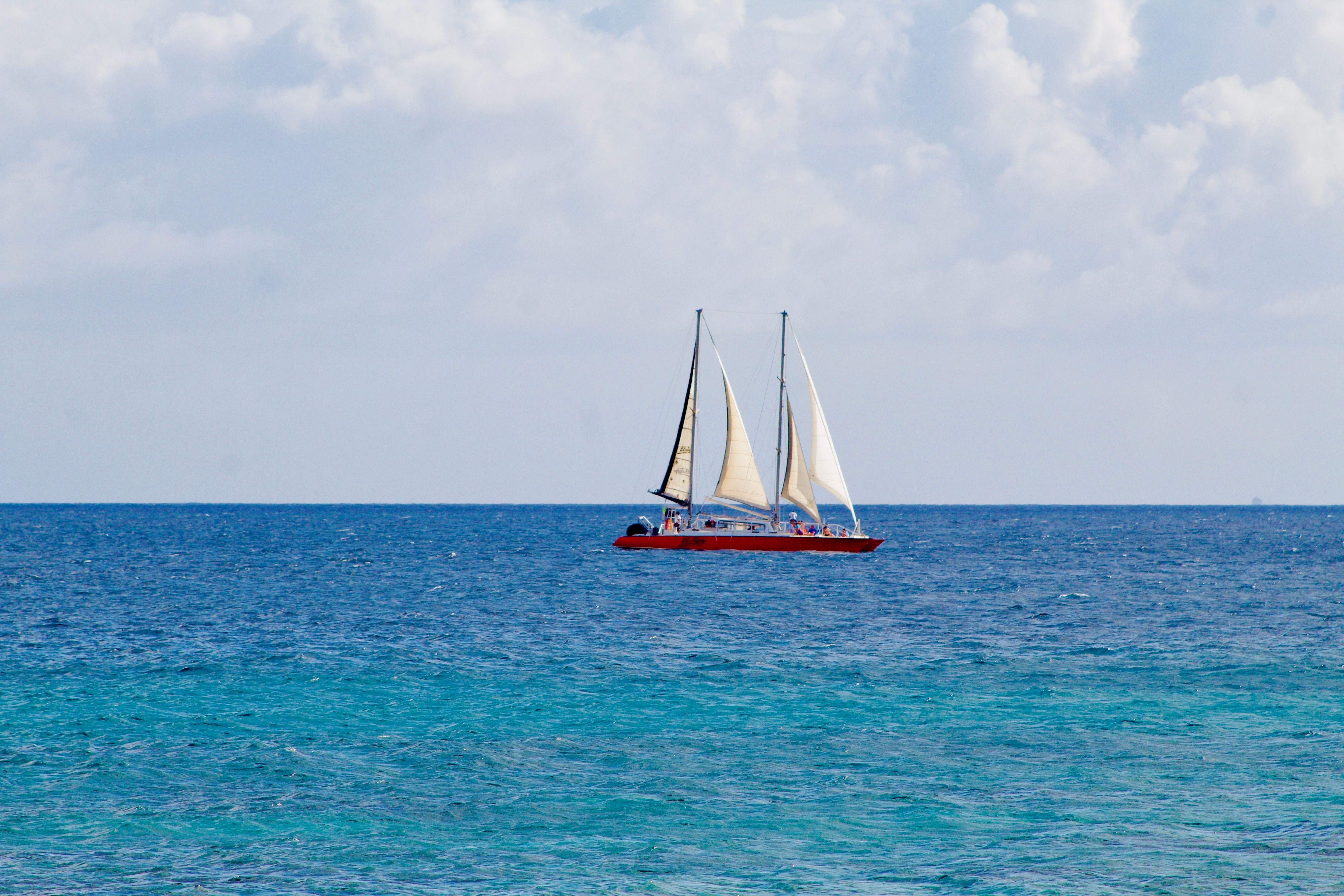 Outstanding Private Afternoon Fishing Charter in Aruba Review: Chasing Big Game on the Caribbean's Best Waters Review 2026 - A red sailboat navigating the tranquil blue ocean under a sky filled with puffy clouds.
