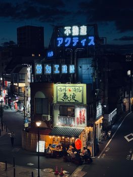 A bustling Tokyo street at night with neon signs and people dining outdoors, capturing urban nightlife.